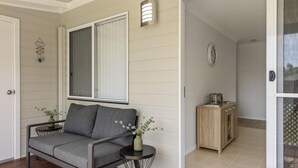 A modern living room with a grey sofa, a small round table with a vase, and a wooden cabinet. - Coastal Soul - Belle Escapes Jervis Bay (Sanctuary Point)