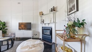 Olohuone, jossa on televisio, takka, valkoiset seinät ja huonekasvi.