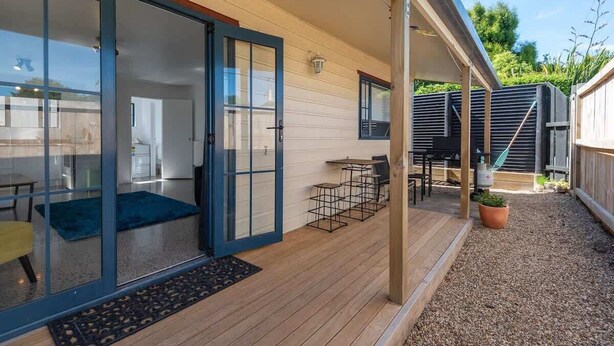 A modern house with a wooden deck, a sliding glass door entrance, and a small outdoor seating area. - Ngongotaha Cottage - Hot Tub, Near Skyline (Rotorua)