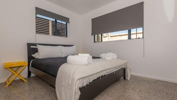 A bedroom with a bed, a small yellow side table, and a window with blinds.