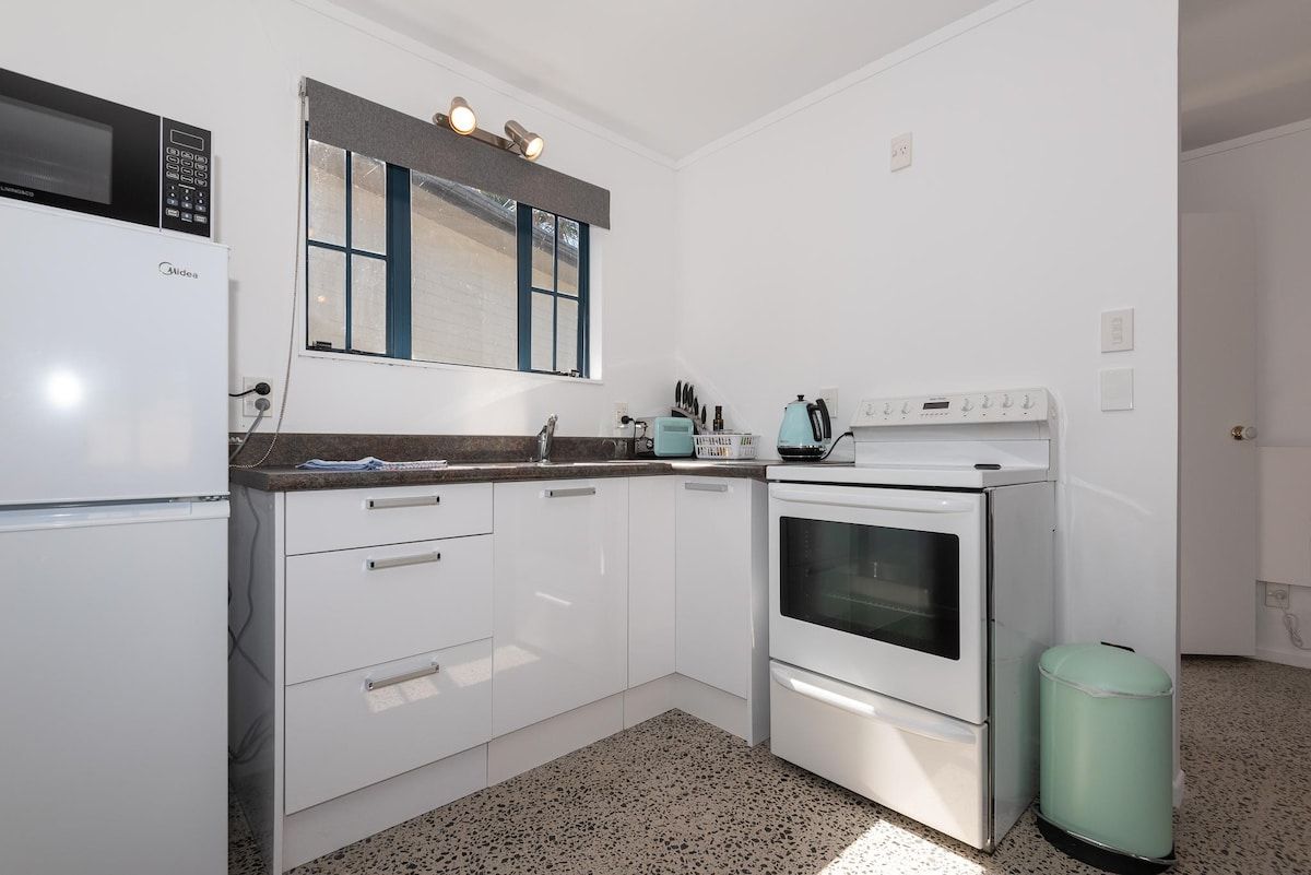 A kitchen with white cabinets, a microwave, a stove, and a trash can.