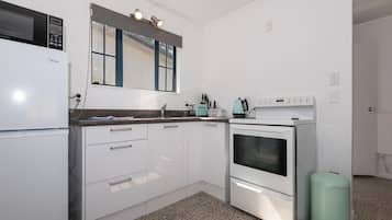 A kitchen with white cabinets, a microwave, a stove, and a trash can.