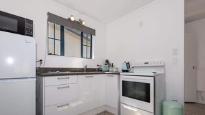 A compact kitchen with white cabinets, a microwave, a stove, and a small trash bin. - Ngongotaha Cottage - Hot Tub, Near Skyline (Rotorua)