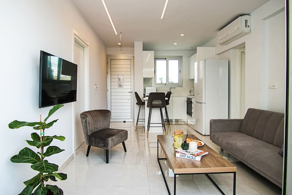 A modern living room with a flat-screen TV, a sofa, a coffee table with magazines, and a potted plant.