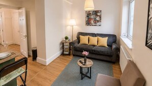 A modern living room with a sofa, a small side table, a lamp, and a painting on the wall. - West Kensington Apt + Garden/wifi near earls court (London)