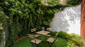 A patio with a wooden table and chairs, surrounded by lush greenery and a white wall. - West Kensington Apt + Garden/wifi near earls court (London)