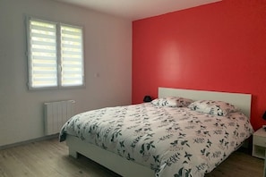 Ein Schlafzimmer mit Bett, Nachttisch, einem Fenster mit Jalousien und einer Heizung.