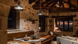 Une pièce rustique aux murs de pierre, avec une table à manger en bois dressée pour un repas, un canapé et une fenêtre offrant une vue agréable.
