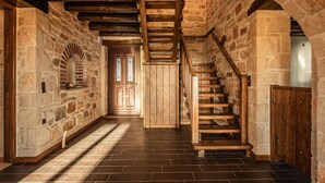 Un couloir aux murs de pierre, avec un escalier en bois menant à une porte dotée de panneaux de verre.