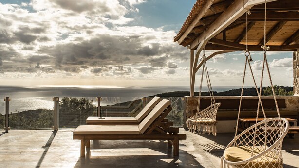 Une terrasse dotée de chaises longues et d’un fauteuil suspendu, offrant une vue sur la côte.