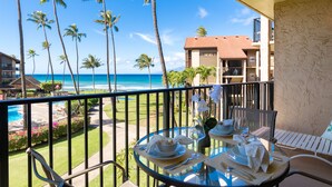 Ein Balkon mit einem Glastisch, gedeckt für ein Essen, mit Blick auf einen Strand, Palmen und den Ozean.