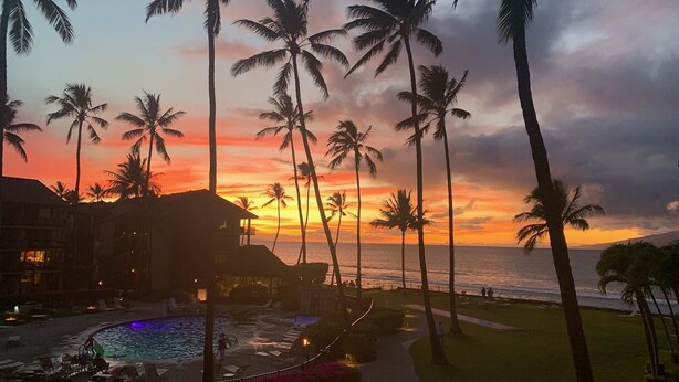 Ein Resort mit Pool, Palmen und Blick auf das Meer bei Sonnenuntergang.