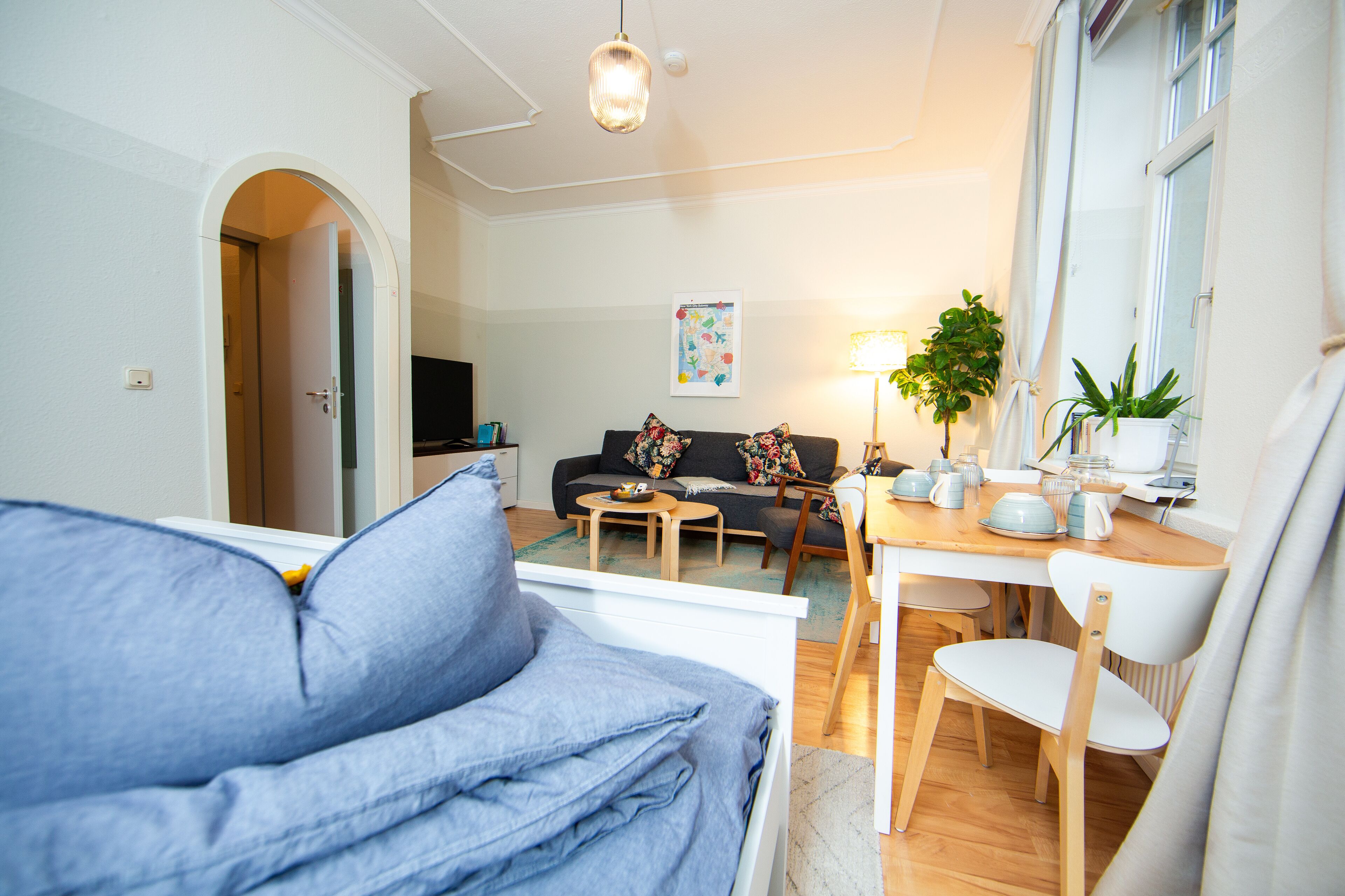 Ein Wohnzimmer mit einer Couch, einem Esstisch mit Stühlen, einem Fernseher und einer Pflanze.
