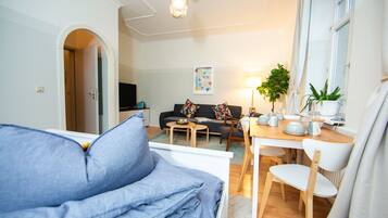 Ein Wohnzimmer mit einer Couch, einem Esstisch mit Stühlen, einem Fernseher und einer Pflanze.