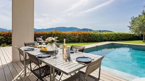 A poolside dining area with a table set for four, overlooking a pool and mountains. - Villa Les Sources VI4245 By Riviera Holiday Homes (Niza)