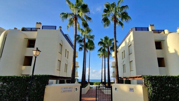 Een hotel met een symmetrische gevel, palmbomen en een heldere lucht.