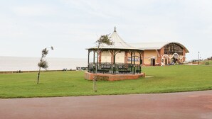 Un gazebo con tetto curvo e base in mattoni, situato in una zona erbosa vicino all'acqua.