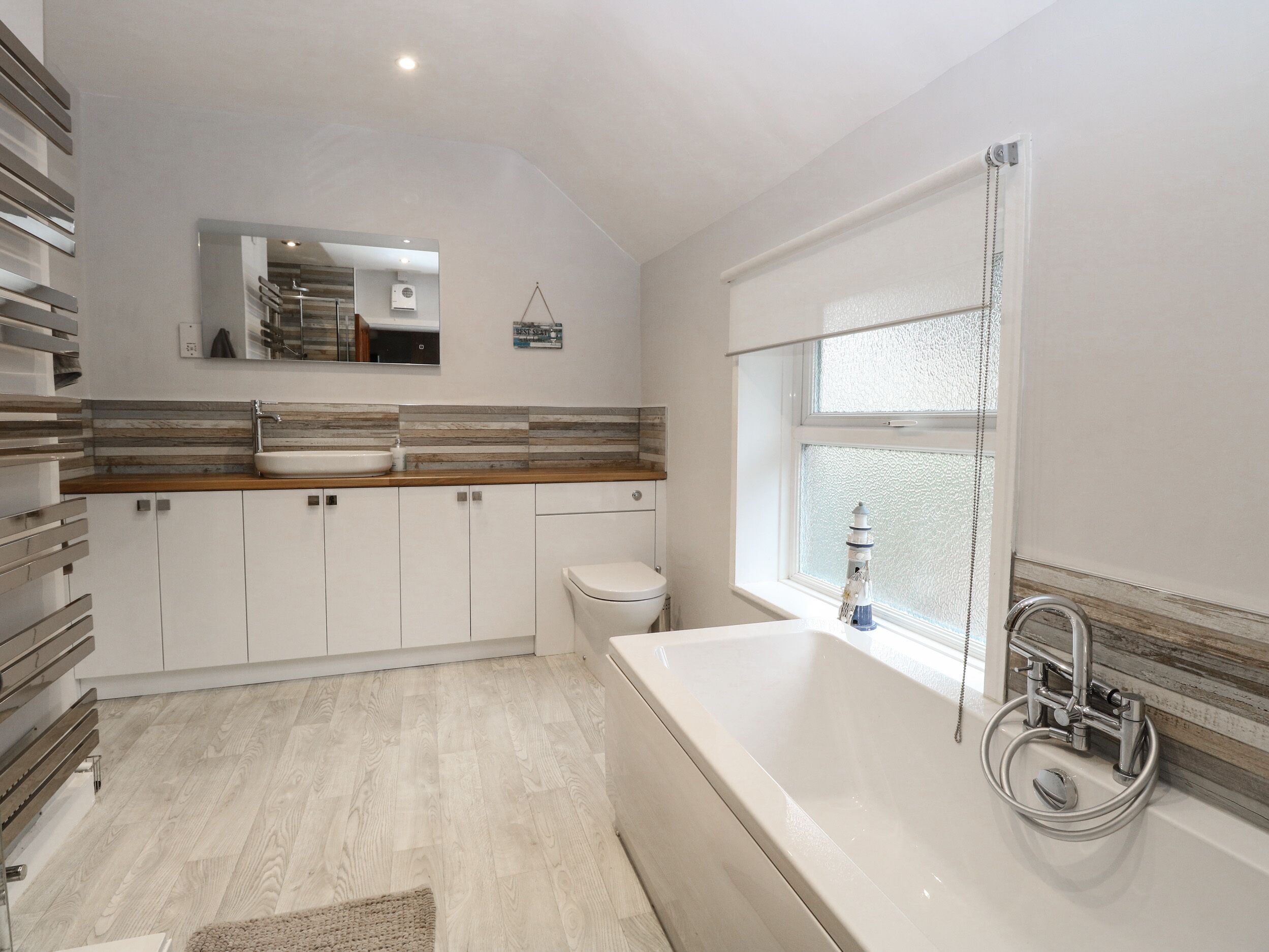 A modern bathroom with a freestanding bathtub, a large mirror, and a window with frosted glass.