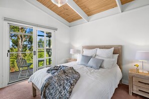 A bedroom with a large bed, a wooden headboard, a nightstand with a lamp, and a view through a sliding glass door to an outdoor deck.