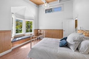 A bedroom with a large bed, a window seat, and a view of greenery outside.