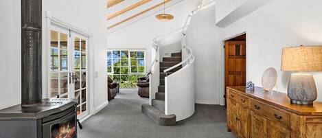 A modern interior with a fireplace, a wooden staircase, and a view of greenery outside.