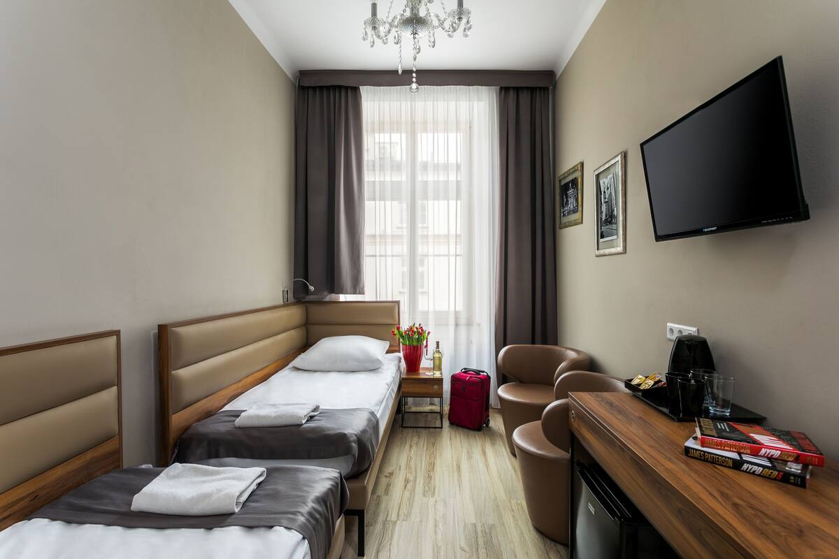 A hotel room with two beds, a desk with a chair, a TV, and a window with curtains.