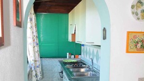 Een smalle keuken met een groene deur, een spoelbak en een klok aan de muur.