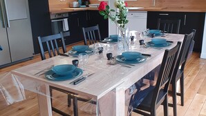 A modern kitchen with wooden cabinets, a dining table set for six, and a vase with flowers on the table. - Single-storey house with private garden and terrace. ANCV, Pets allowed (ST LUNAIRE)