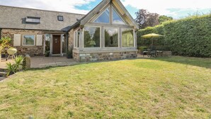 A stone house with a large glass bay window, a patio with outdoor furniture, and a well-maintained lawn. - Swallows Barn (Chesterfield)