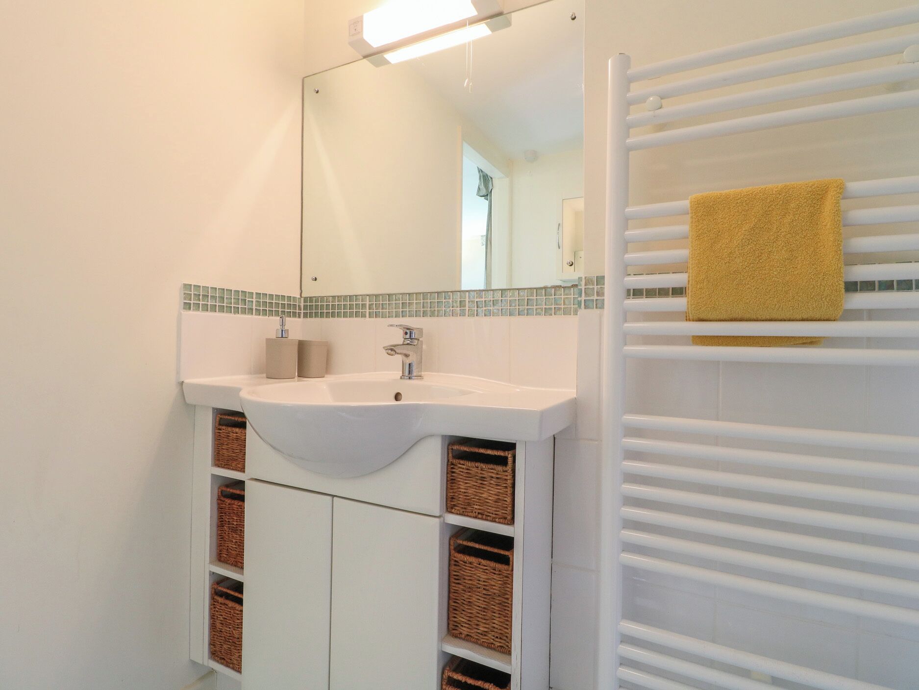Un baño con lavamanos blanco, espejo y perchero para toallas.