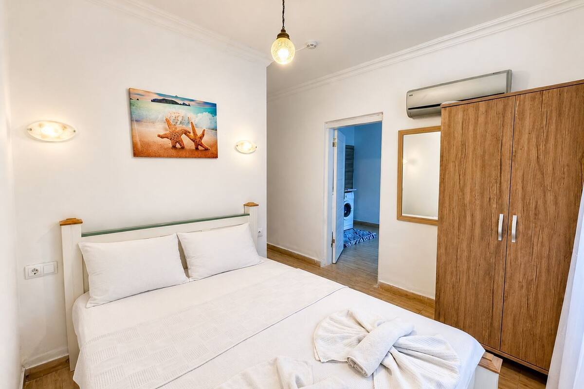 A bedroom with a bed, a wooden wardrobe, a painting, and an air conditioning unit.