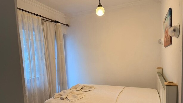 Une chambre à coucher avec un lit, une lampe suspendue, une fenêtre avec des rideaux et un tableau accroché au mur.
