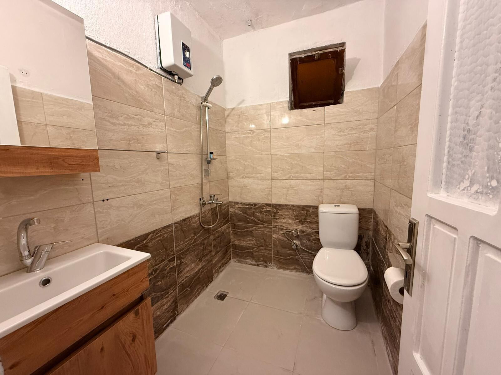 Baño con lavabo, inodoro, ducha y una ventana pequeña.
