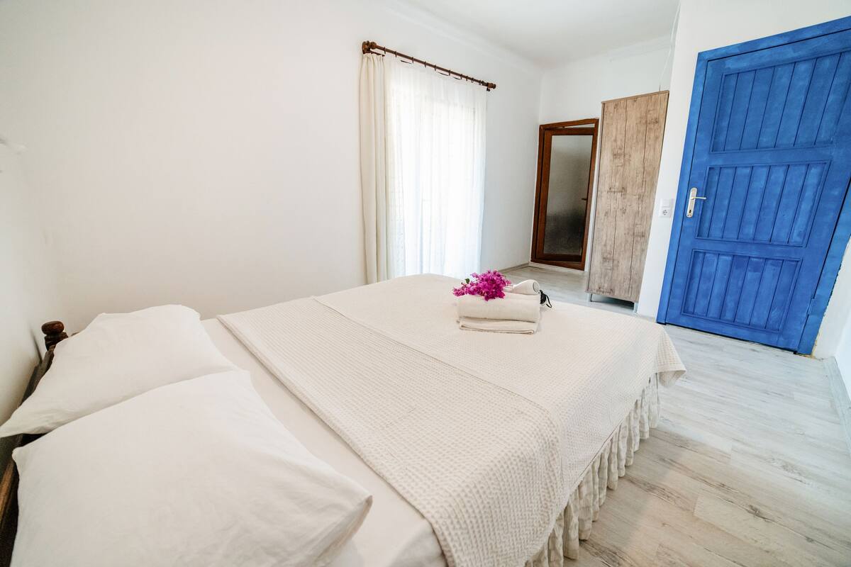 A bedroom with a bed, white linens, a wooden door, and a blue door.