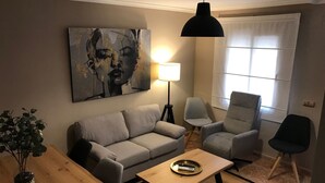 En stue med sofa, lænestole, sofabord, lampe og et maleri på væggen.