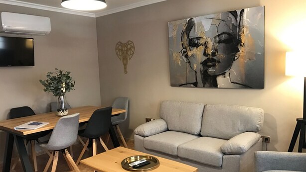 En moderne stue med en grå sofa, et træbord som sofabord og et spiseområde med et træbord og stole.