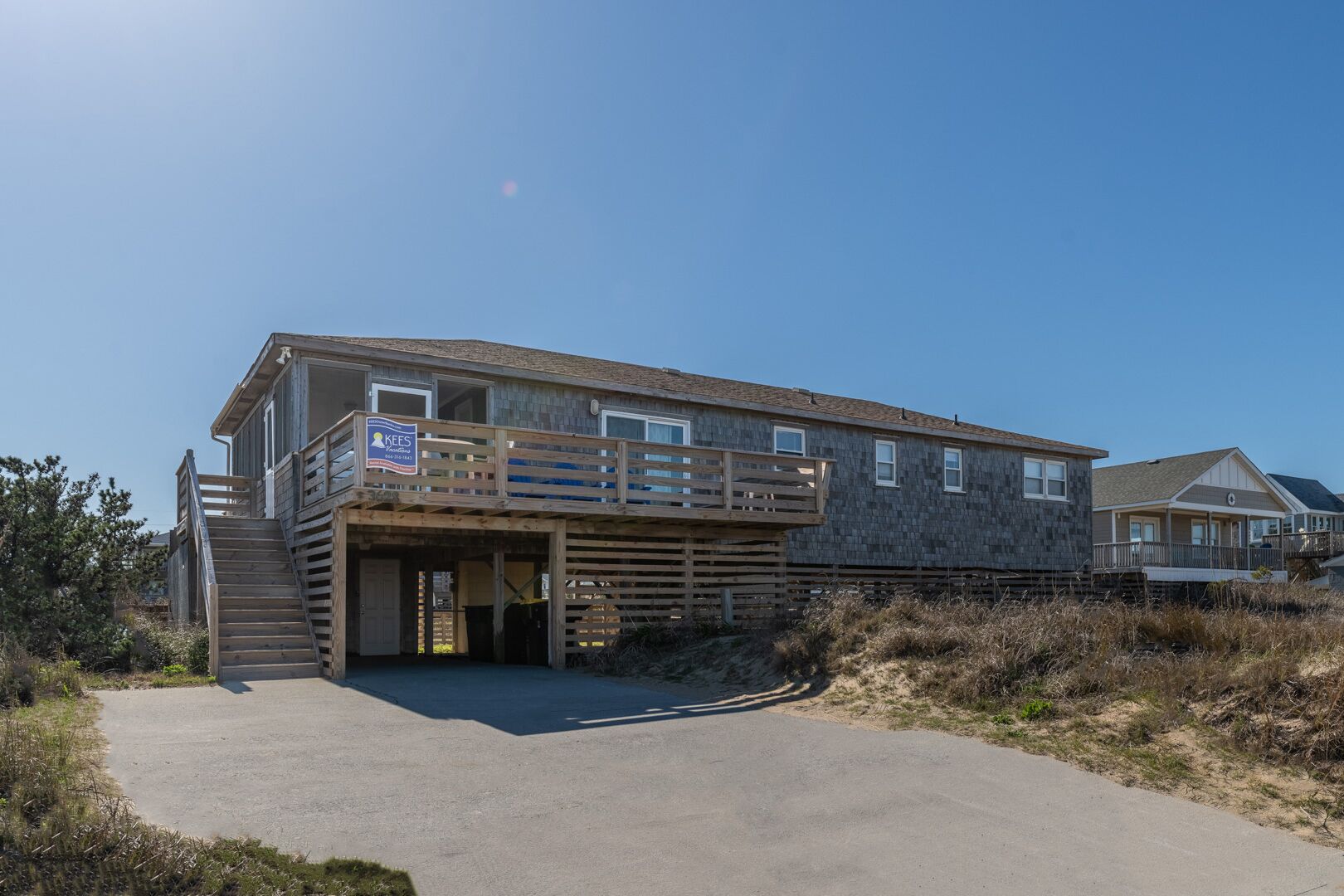 Ett tvåvåningshus vid stranden med en träveranda och en inglasad entré.