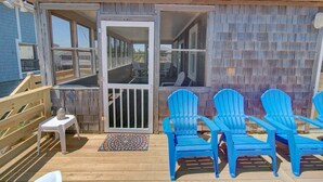 A wooden deck with blue Adirondack chairs, a small table, and a door leading to an interior space. - Dawn Patrol 4 Bedroom Home in Kitty Hawk (Kitty Hawk)