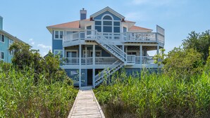 Una casa frente al mar de dos pisos con una terraza de madera que conduce a un balcón.