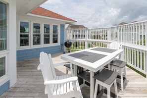 Een overdekt terras buiten, met een tafel, stoelen, een barbecue en een witte omheining.
