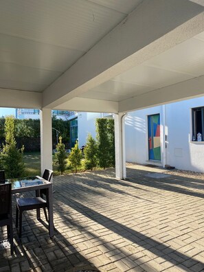 Relax in the serene outdoor patio, surrounded by lush greenery and a modern building with a unique door design.