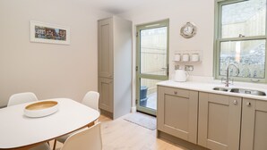 A modern kitchen with a dining area, featuring a white table and chairs, a built-in oven, and a window with a view of a wooden fence. - Kimberlin (Portland)