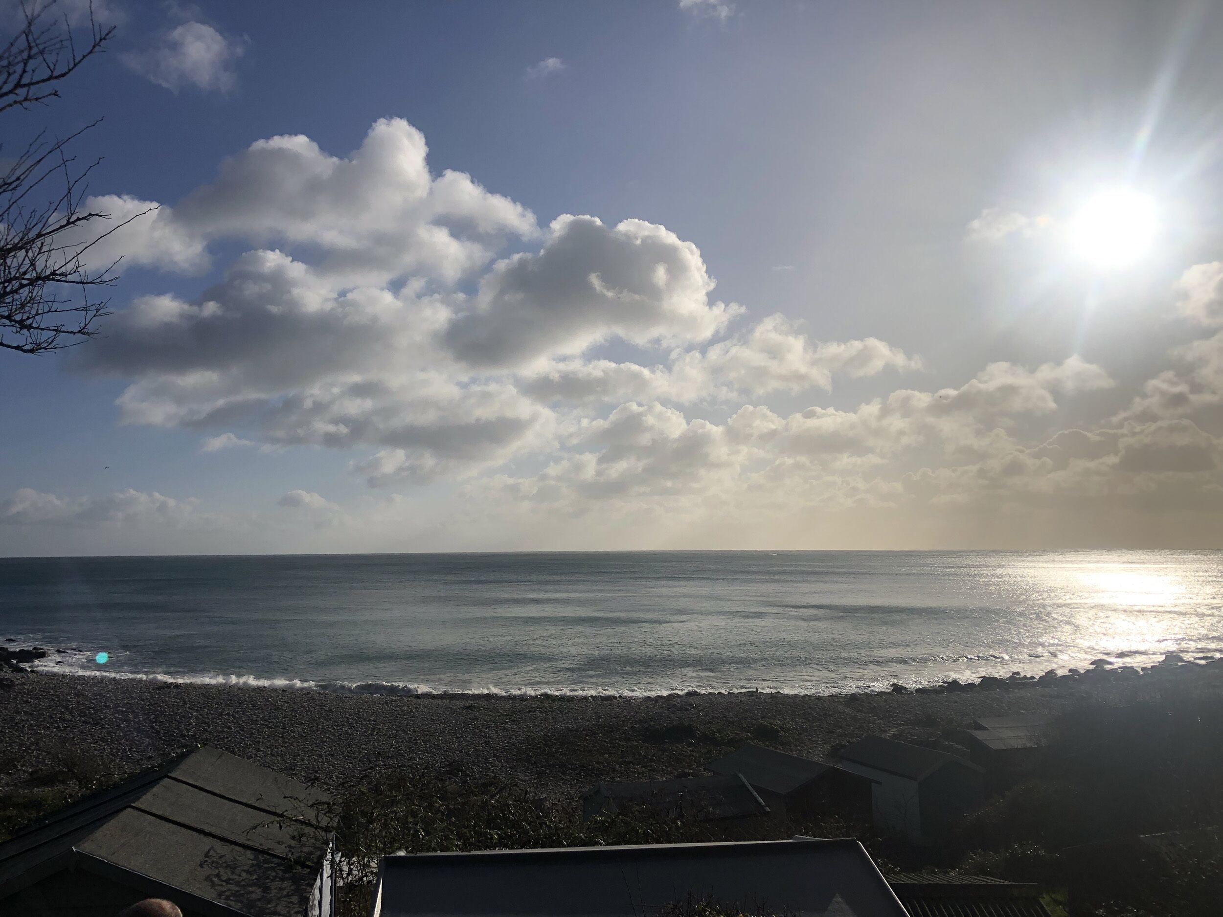 Blick auf einen Strand bei Sonnenuntergang über dem Meer, eine felsige Küstenlinie und einige Gebäude im Vordergrund.