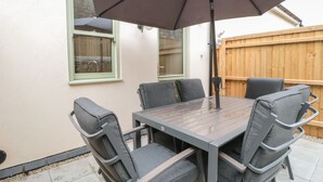Un patio con una mesa, sillas, un paraguas y una cerca de madera al fondo.