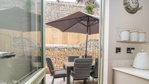 A patio area with a table and chairs, a large umbrella, and a stone wall in the background. - Kimberlin (Portland)