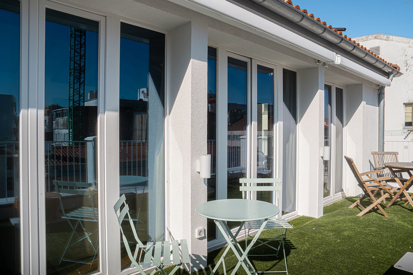 Un patio techado al aire libre con mesa y sillas, un pequeño jardín y vistas de los edificios circundantes.