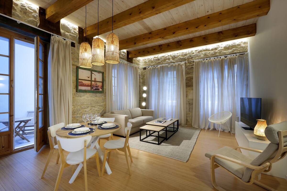 Ein gemütliches Wohnzimmer mit Holzbalkendecke, einer Couch, einem Esstisch mit Stühlen und einem Fernseher.