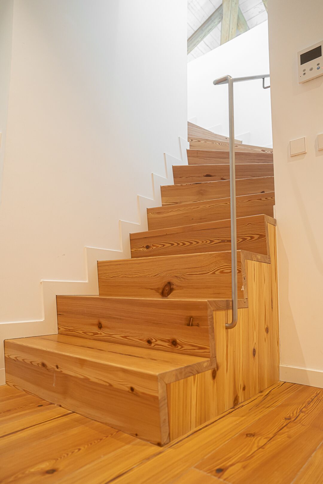 A wooden staircase with a metal handrail, white walls, and a wooden floor.