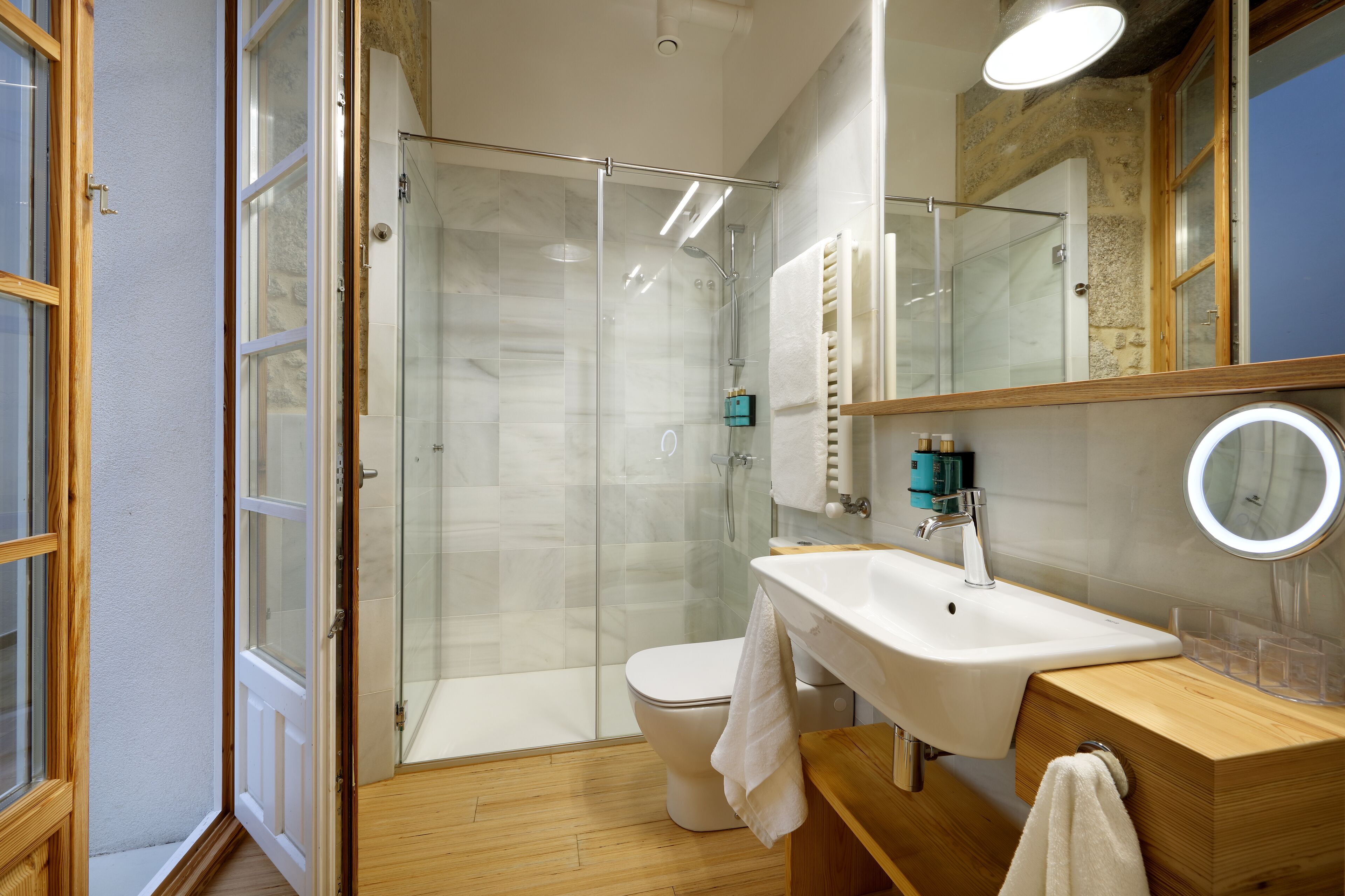 A modern bathroom with a glass-enclosed shower, a white sink, and a wooden vanity.