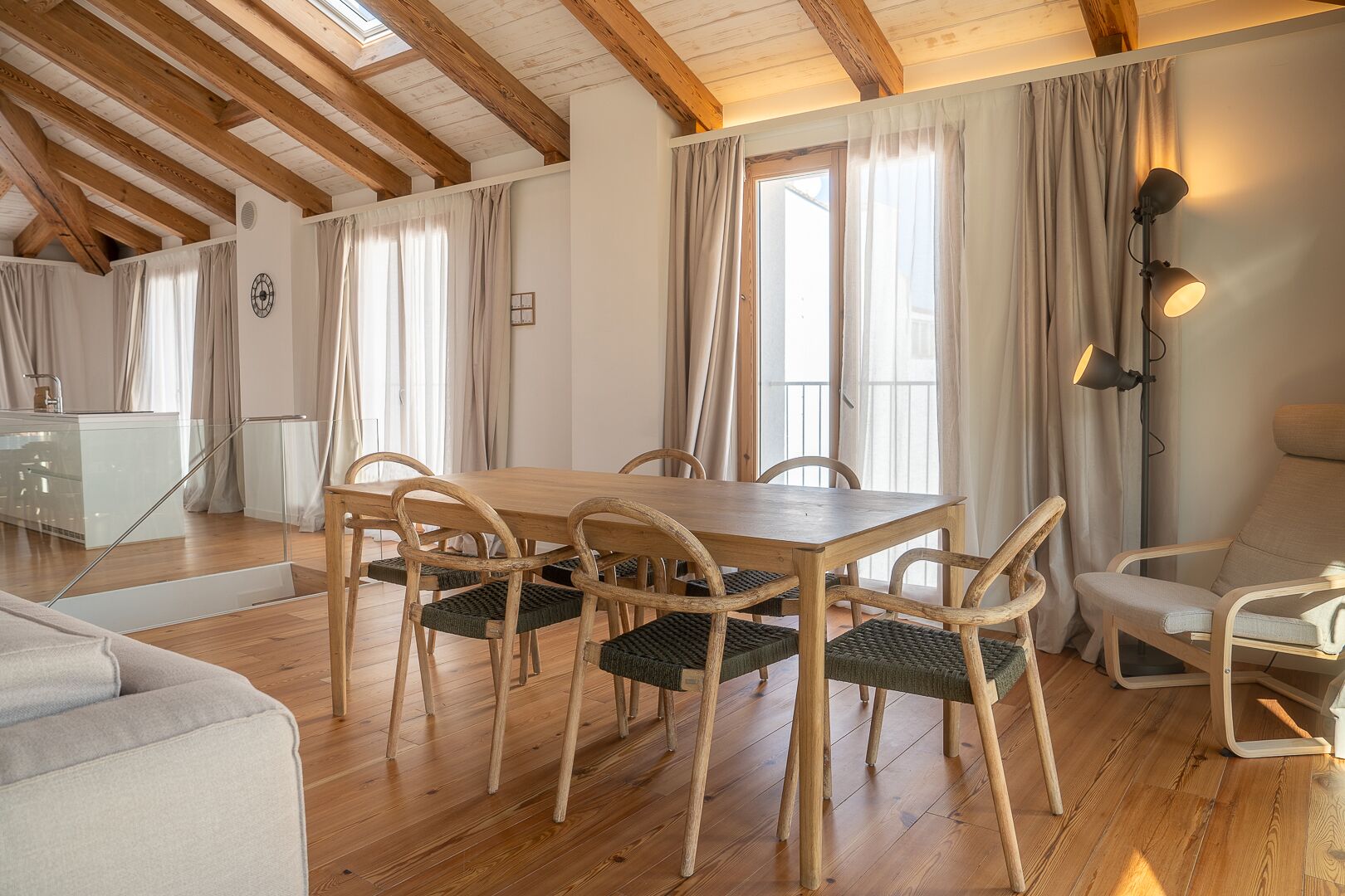 A dining area with a wooden table and chairs, a sofa, and a lamp.